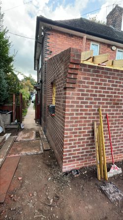A red brick house extension under construction with roof joists and decorative corbelled brickwork on the corner