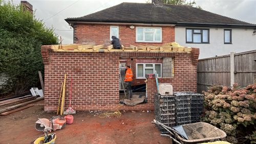 Builders working on a red brick house extension with wooden roof joists being installed