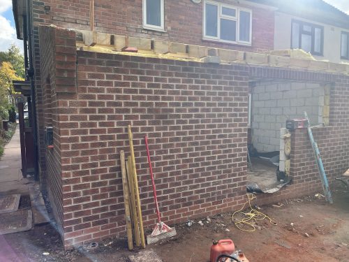 A red brick house extension under construction with wooden roof joists and insulation